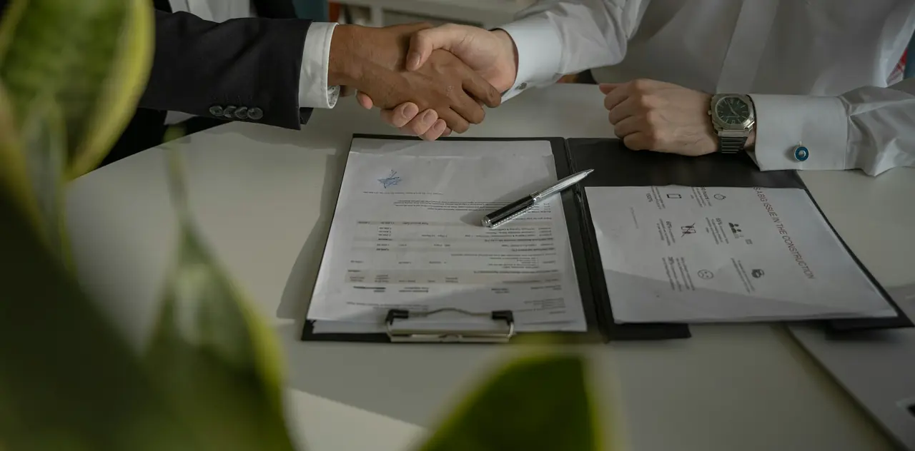 Handshake across a desk over signed documents