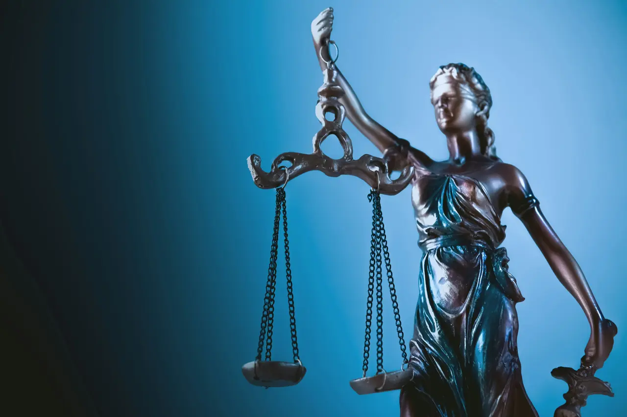 Statue of Lady Justice holding scales against a blue background